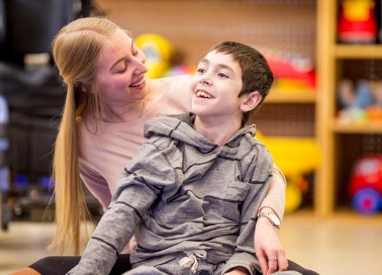 Boy with brown hair and big smile sits on floor with smiling woman with blond hair
