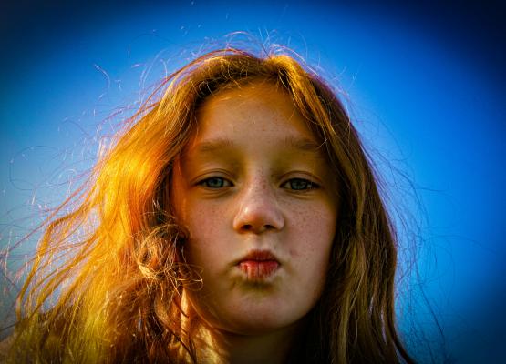 Girl with red hair purses lips on blue background
